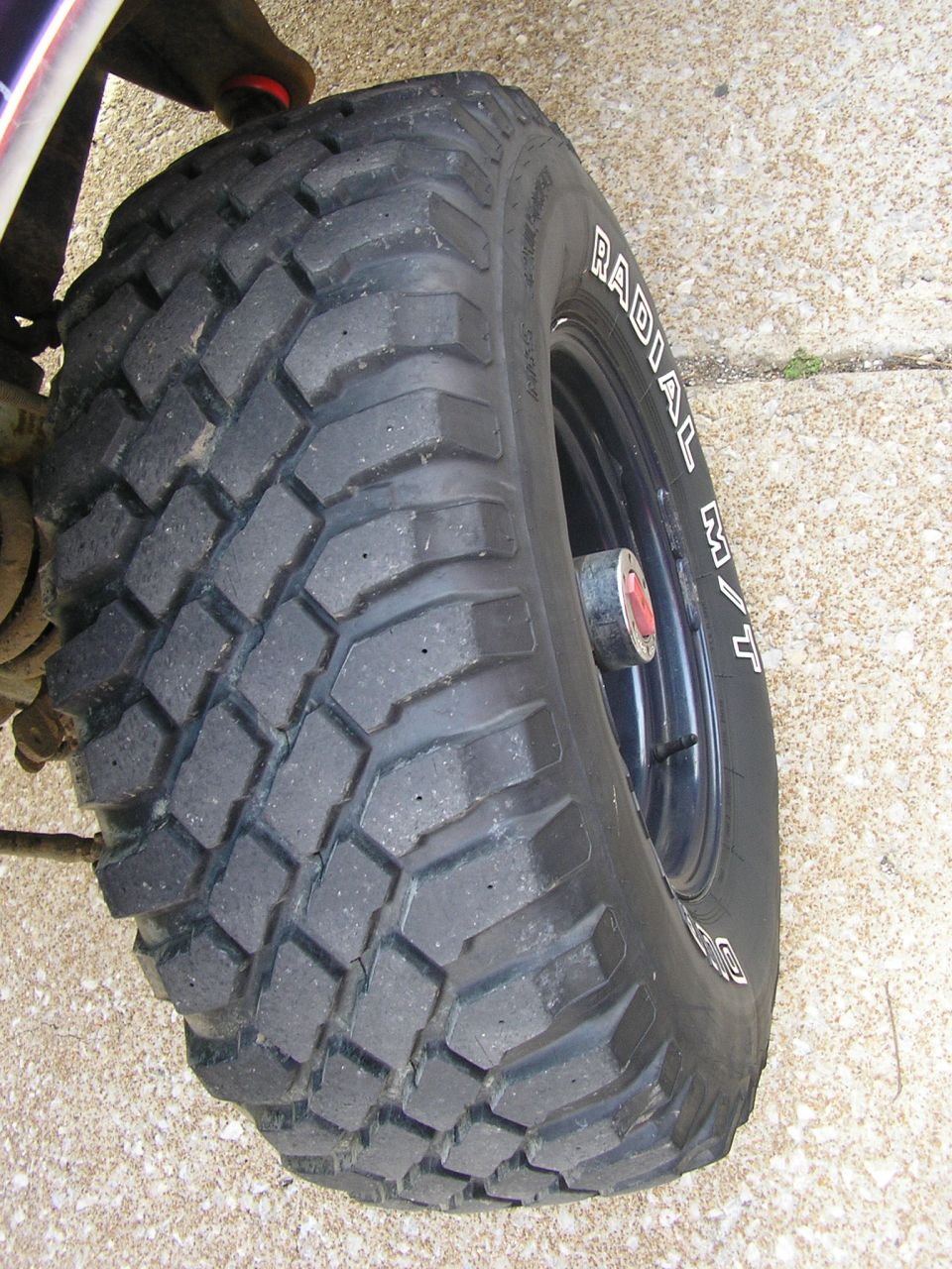 Radial M/T mud tire on black wheel with red center cap, brake and suspension visible