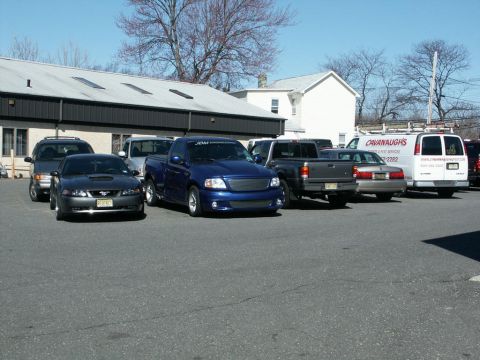 2001 Mercury Grand Marquis - Several trucks and cars are parked in a lot outside a building on a sunny day.