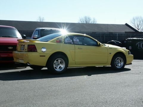 2001 Mercury Grand Marquis - A yellow Ford Mustang is parked next to other vehicles, displaying numerous racing decals on its side.