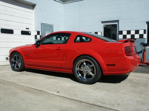 2001 Mercury Grand Marquis - A red Ford Mustang is parked in front of a garage door, showing off its custom wheels and spoiler.