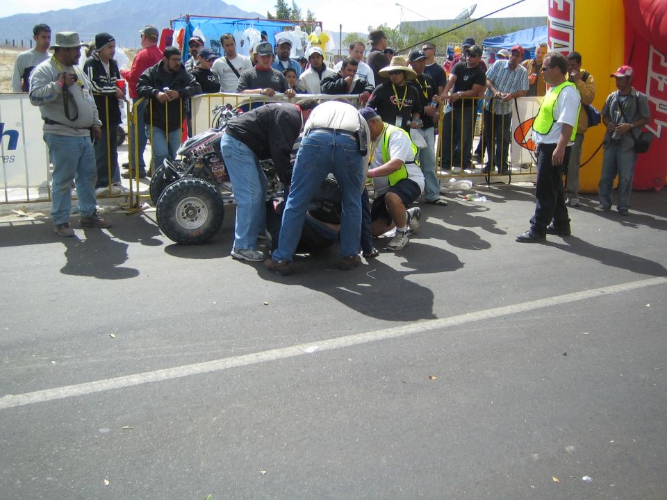 Group of people crouched around a racing quad on a paved street with long shadows