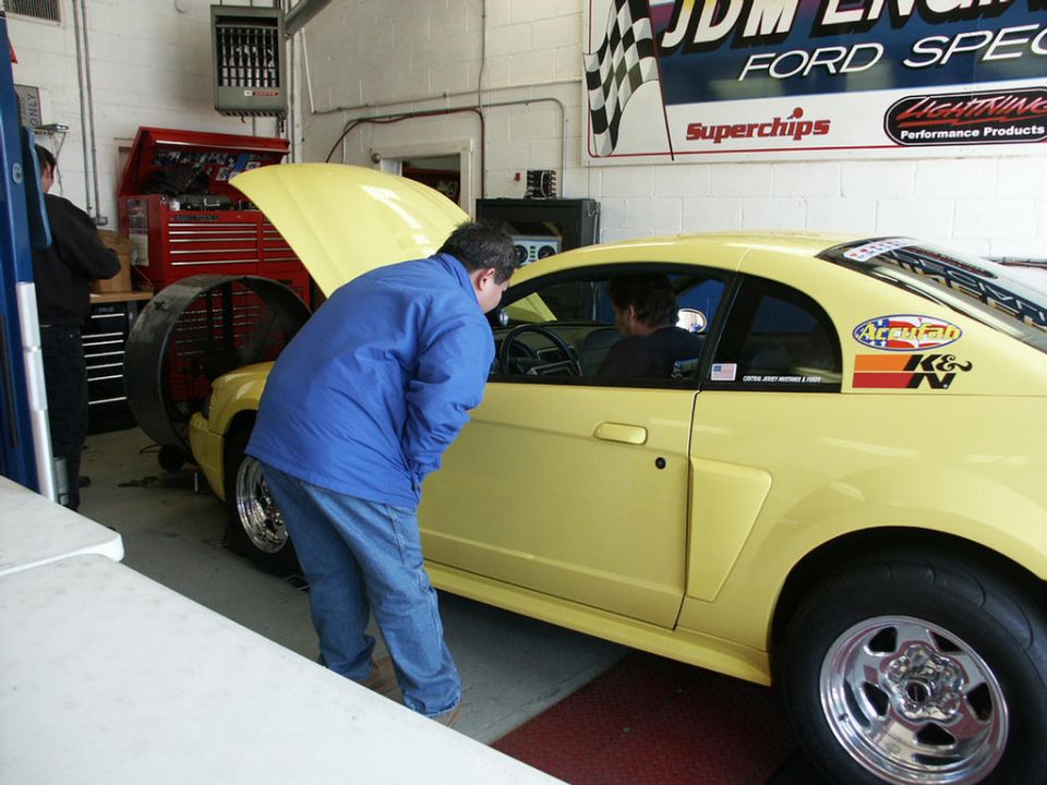 Yellow Ford Mustang on a dyno, hood up, guy looking in window. K&N sticker on rear quarter panel
