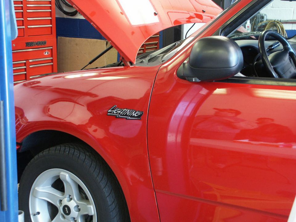 Red pickup truck with 'Lightning' badge on fender, hood open, in a garage