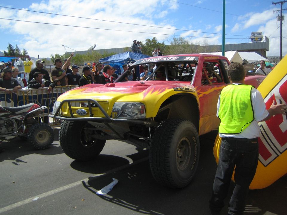 Red and yellow flame-painted off-road race truck on a street with a worker in a yellow vest