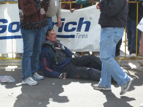 1990 Ford Bronco - racer in chest armor rests on the pavement against a BFGoodrich Tires banner as bystanders in jeans stand around him.