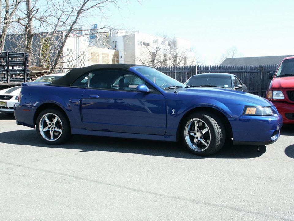 Blue convertible sports car parked outside, with a white car and red truck nearby