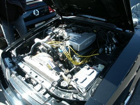 2001 Mercury Grand Marquis - Close-up of a Ford Mustang engine bay with the hood open. A second Mustang is parked behind it.