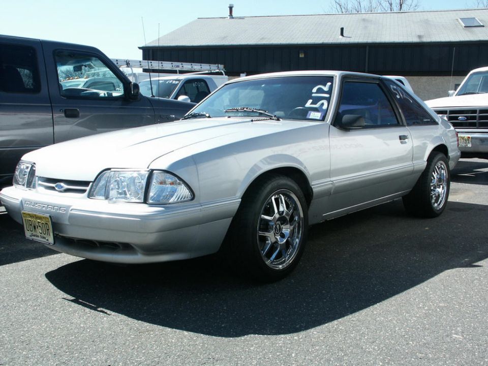 Silver Ford Mustang with chrome wheels parked next to a dark pickup truck