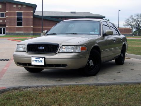 2000 Ford Crown Victoria - A tan 2000 Ford Crown Victoria is parked in front of a brick building.