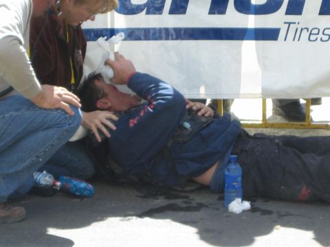 1990 Ford Bronco - Medics press a dressing to the head of an injured racer lying on the pavement against a banner, water bottles nearby.