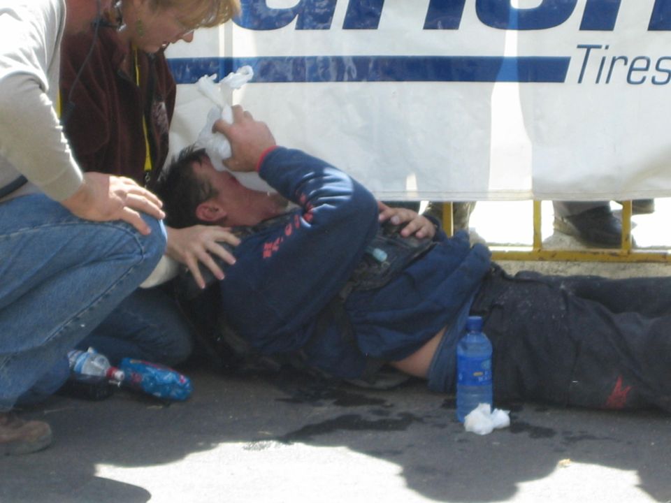 Medics tending an injured racer lying on the ground with water bottles and a head bandage