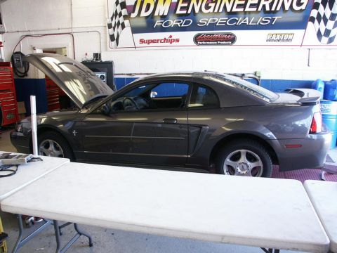 2001 Mercury Grand Marquis - A dark gray Ford Mustang is parked inside a garage with its hood open, under a banner for JDM Engineering.