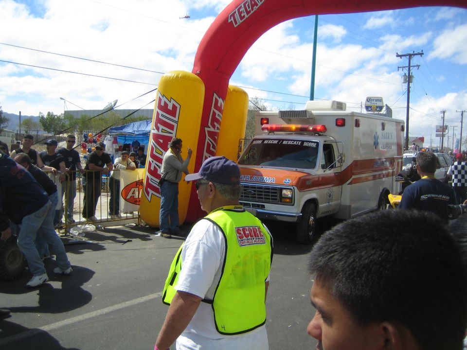 Orange and white ambulance and a yellow Tecate inflatable arch at a desert race with a SCORE official