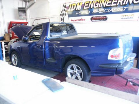 2001 Mercury Grand Marquis - A blue Ford F-150 SVT Lightning is positioned on a dynamometer with its hood open, inside a workshop.