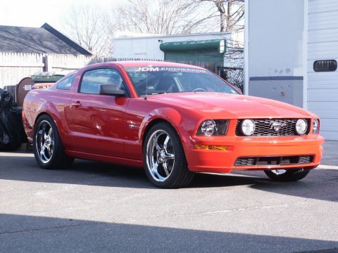 2001 Mercury Grand Marquis - A red Ford Mustang coupe is parked outside a building with a green garage door.