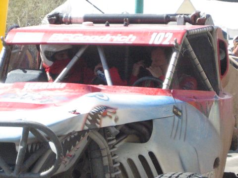1990 Ford Bronco - Red BFGoodrich off-road race truck 102 with shark-mouth nose art carries two helmeted occupants behind the cage.