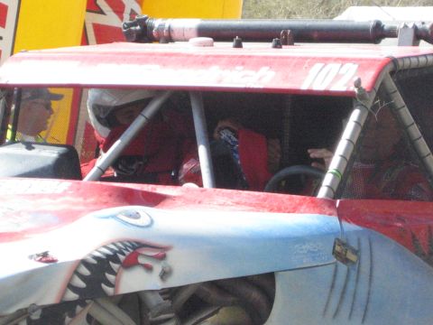 1990 Ford Bronco - red number 102 off-road race buggy with a helmeted driver in the roll cage and shark-mouth artwork painted on its silver nose.