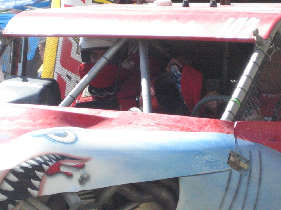 Red off-road race buggy with driver and passenger in roll cage, shark-mouth nose art, number 102