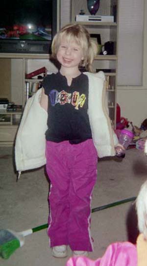 2002 Oldsmobile Aurora - A smiling child stands indoors, dressed in casual clothing and a jacket, with a television and shelves in the background.