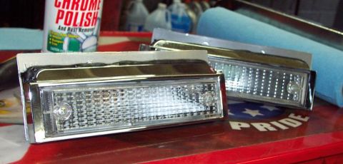 1985 Ford Crown Victoria LTD - Headlight assemblies with chrome trim and clear lenses are displayed next to chrome polish and a blue foam roller.