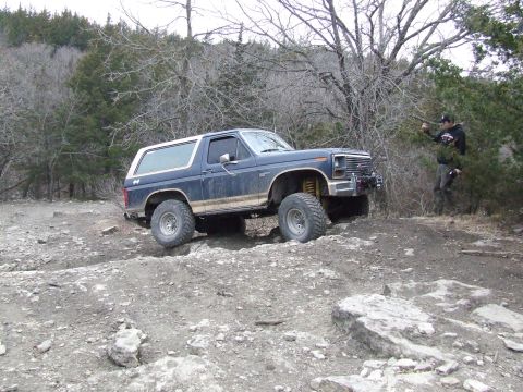 1986 Ford Bronco - A Ford Bronco navigates a challenging rocky trail with a person observing in the background.