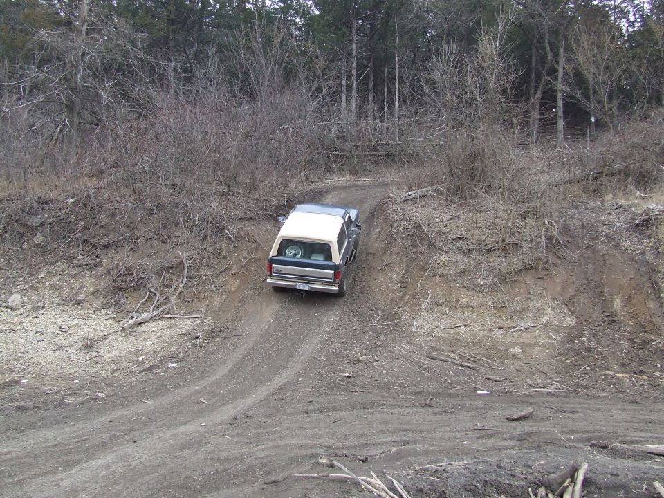 Two-tone Ford Bronco driving up a dirt hill, tan canopy over blue body