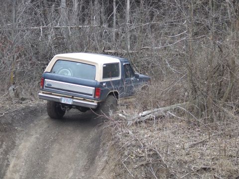 1986 Ford Bronco - This 1986 Ford Bronco navigates a rough dirt trail surrounded by bare trees.