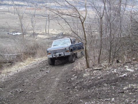 1986 Ford Bronco - Ford Bronco navigates a rough, wooded terrain on a dirt path.