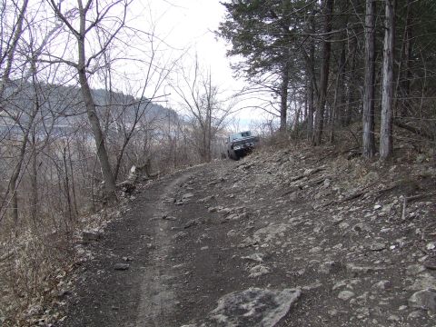 1986 Ford Bronco - A vehicle navigates a challenging, rocky path surrounded by bare trees on a cloudy day.