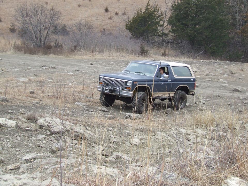 Dark blue Ford Bronco with a white top drives on a rocky, dry terrain