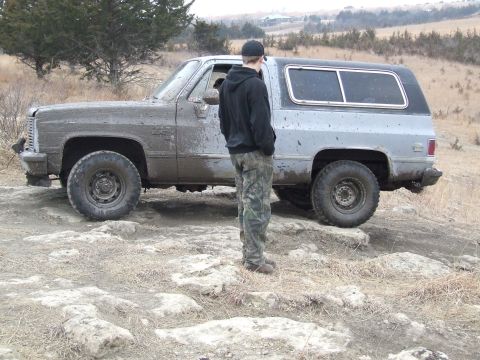 1986 Ford Bronco - A mud-splattered SUV is parked on rocky terrain, with a person standing beside it.