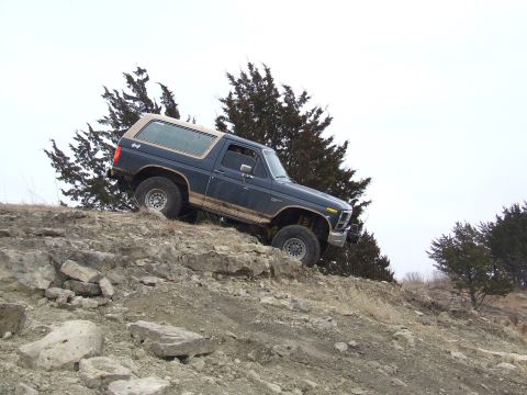 1986 Ford Bronco - This SUV navigates a rocky incline under an overcast sky.