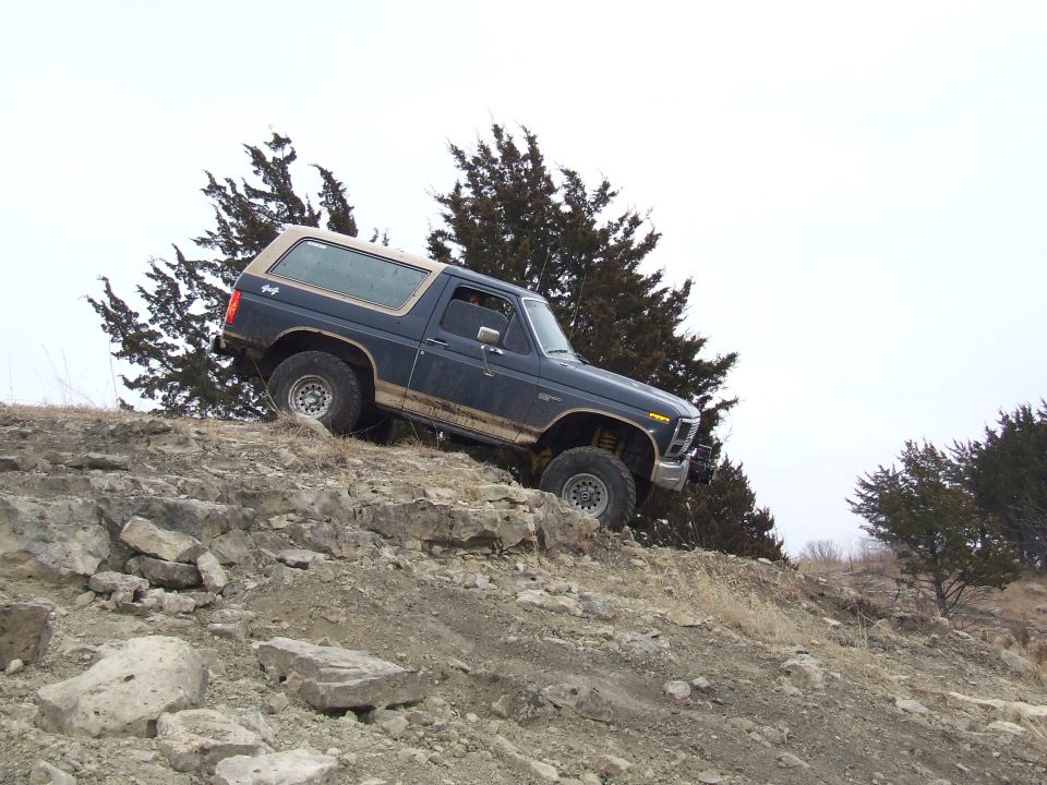 Dark blue SUV with tan top climbing rocky terrain, mud on lower body