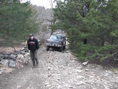 1986 Ford Bronco - Man and 1986 Ford Bronco on a rocky trail surrounded by trees.
