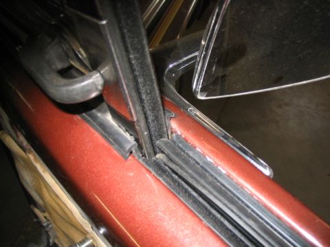 1979 Ford Bronco - Close-up of a car's door frame and window seal, showing the metallic red paint and chrome accents.
