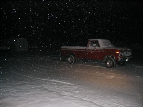 1979 Ford Bronco - A red pickup truck is seen in a snowy landscape at night while snow falls.