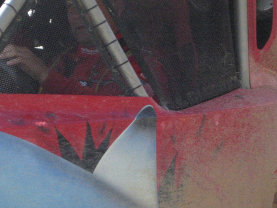 Close-up of weathered red and silver bodywork on an off-road race buggy with roll cage and mesh