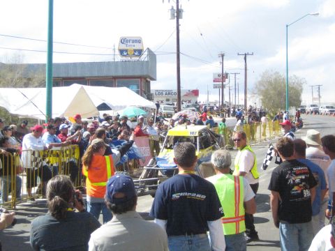 1990 Ford Bronco - Spectators line a barricaded street watching a yellow off-road buggy, with a Corona sign and Los Arcos restaurant in the background.