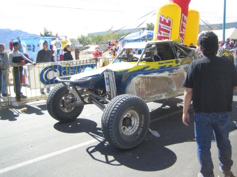 1990 Ford Bronco - blue and white tube-frame off-road race buggy sits on a street near a Tecate inflatable as a man in a black shirt approaches it.