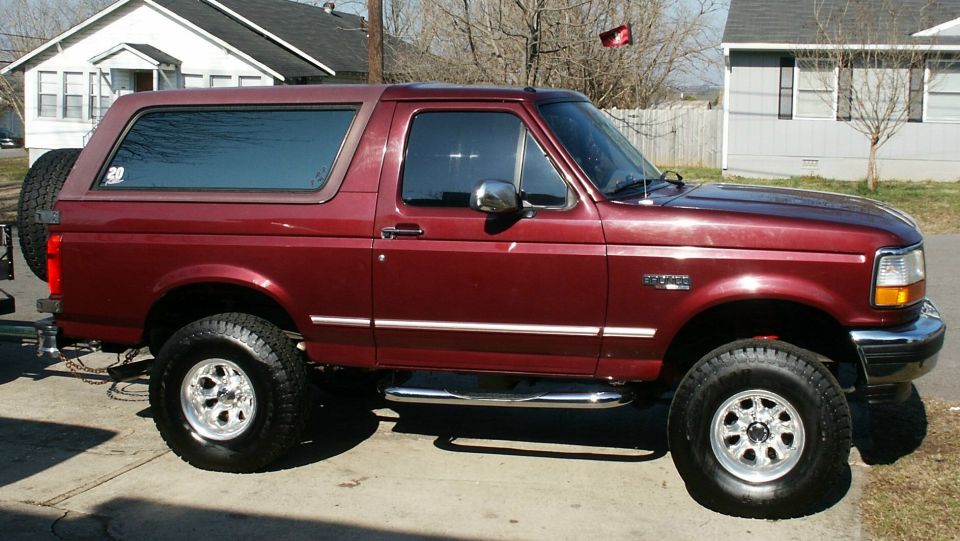 Side view of a lifted maroon Ford Bronco SUV with chrome wheels and step bars parked in a driveway
