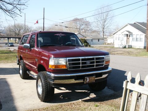 1996 Ford Bronco - Maroon 1996 Ford Bronco parked on a driveway with houses in the background.