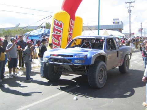 1990 Ford Bronco - blue and silver off-road trophy truck with a Chevrolet-style front end sits at the start line beside a yellow Tecate inflatable.