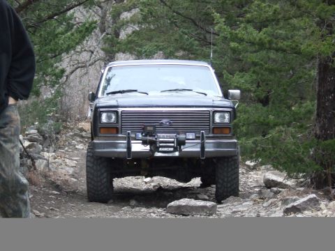 1986 Ford Bronco - This Ford Bronco is navigating a rough, off-road path surrounded by trees and rocks.