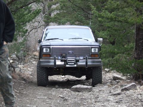 1986 Ford Bronco - A 1986 Ford Bronco navigates a rocky trail, equipped with a front-mounted winch for off-road challenges.