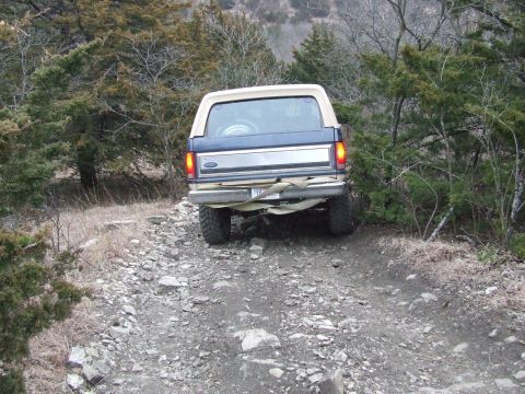 1986 Ford Bronco - A Ford Bronco navigates a rough, off-road path surrounded by trees.