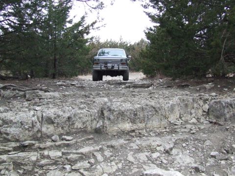 1986 Ford Bronco - A 1986 Ford Bronco navigates a , rocky terrain, seen from the rear.