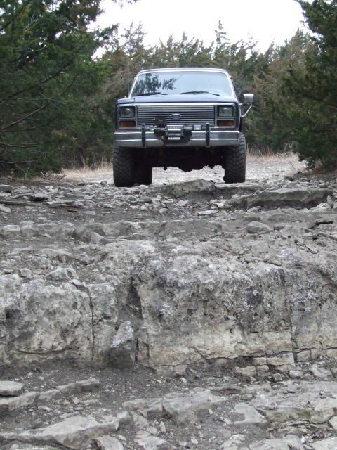 1986 Ford Bronco - 1986 Ford Bronco navigating a rocky trail with trees in the background.