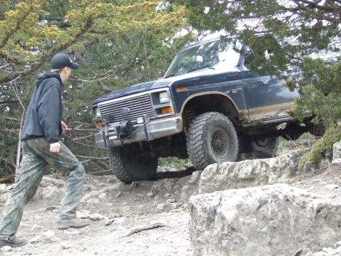 1986 Ford Bronco - A man walks near a dark blue Ford Bronco navigating a rocky off-road path.