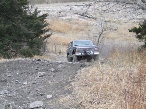 1986 Ford Bronco - 1986 Ford Bronco navigating an off-road trail with a rocky surface and sparse vegetation.