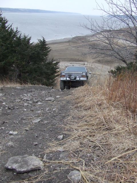 1986 Ford Bronco - A Ford Bronco navigates a rocky, off-road trail with a large body of water in the background.